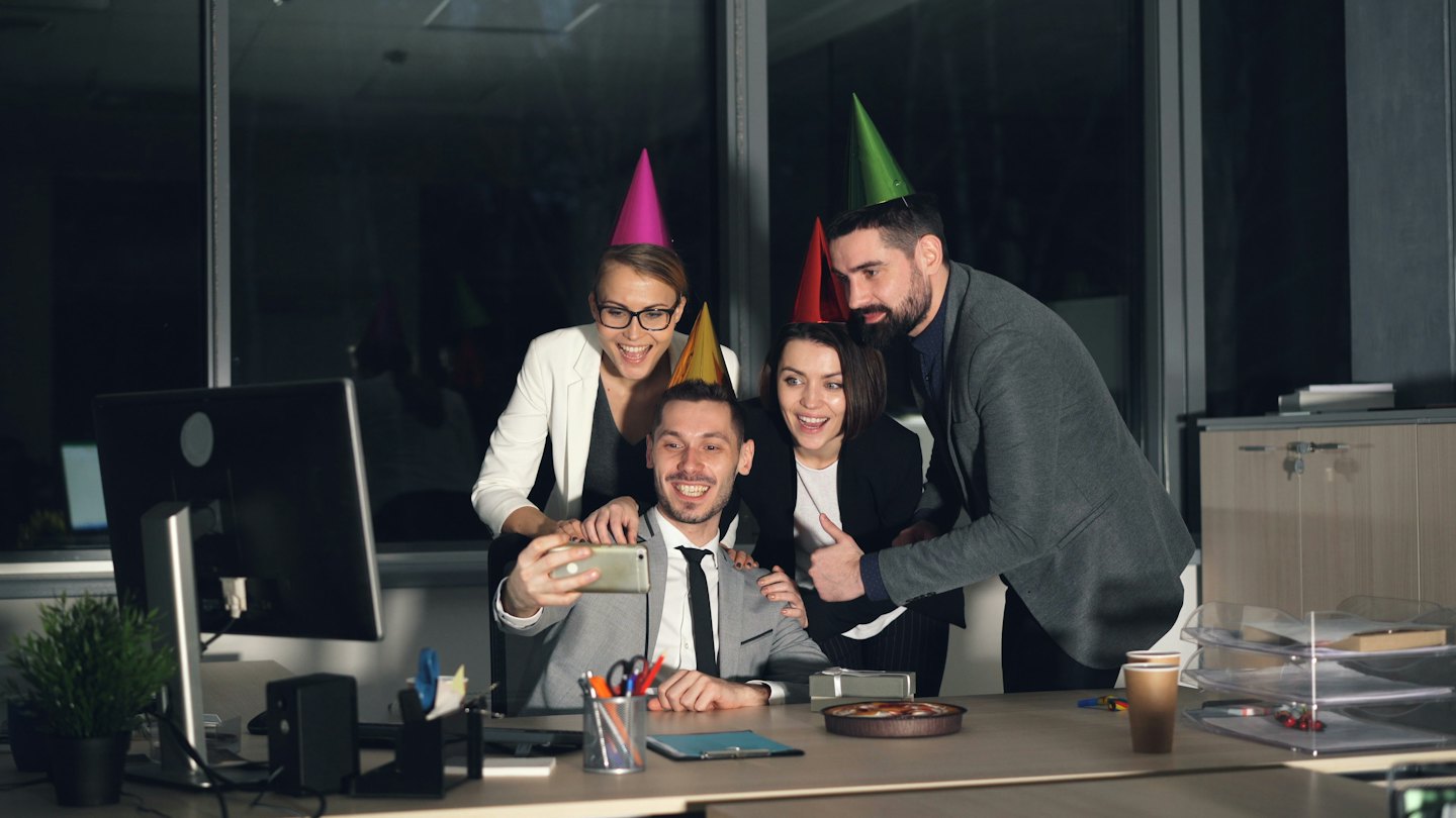 Des collègues en chapeaux de fête prennent un selfie de célébration au bureau.