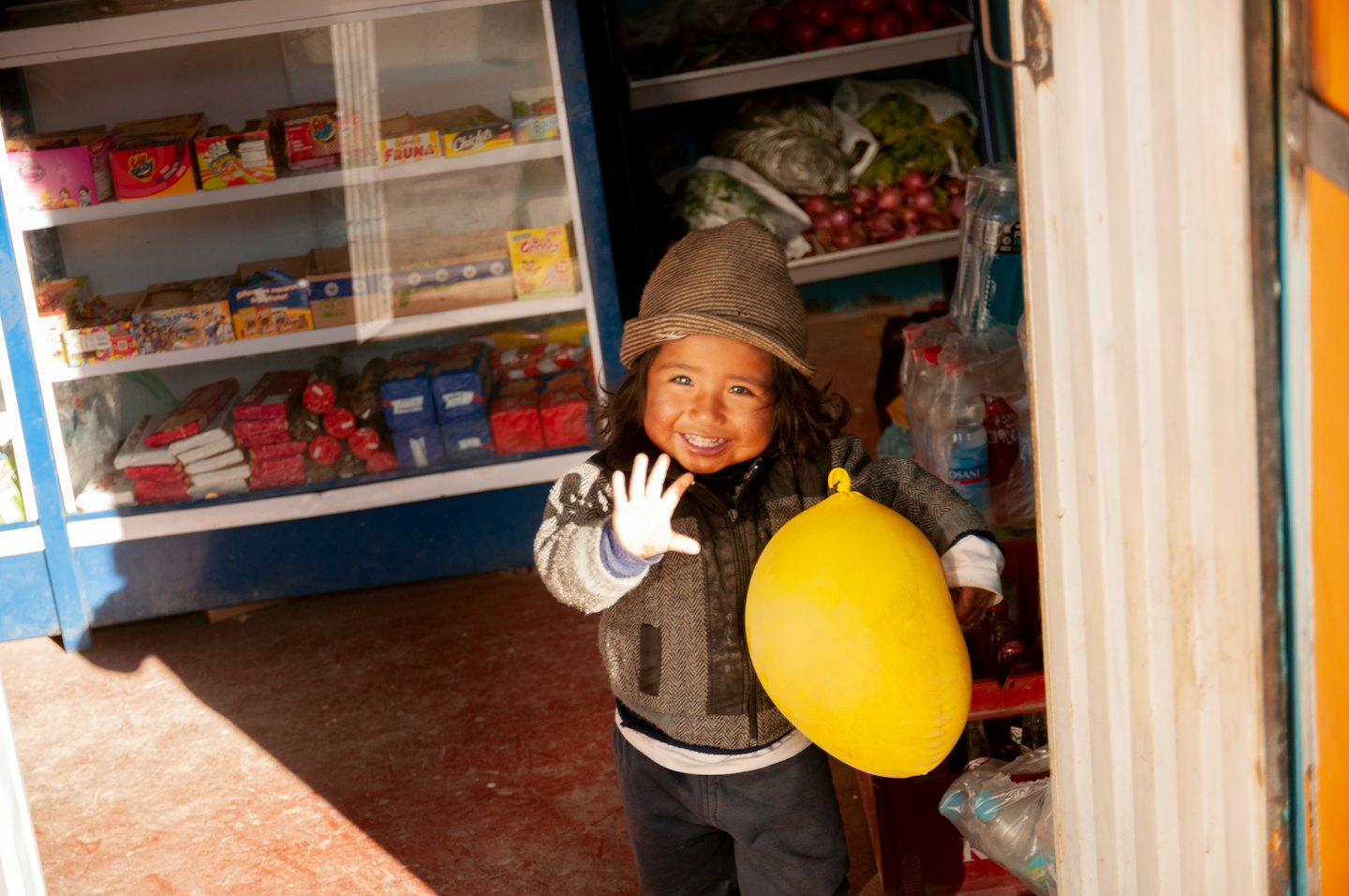 Enfant au bonnet rayé agitant un ballon jaune.