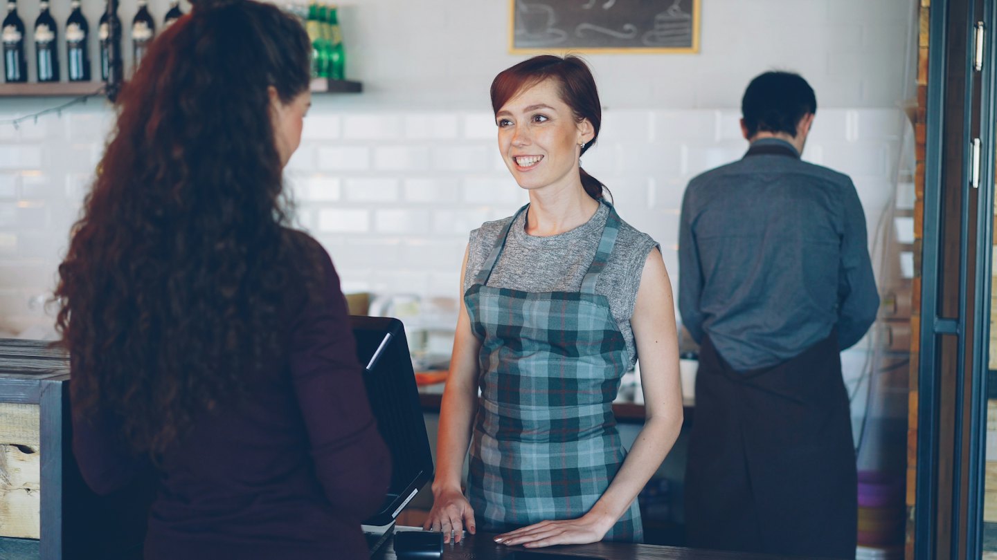 Un employé de café sourit en servant un client au comptoir.