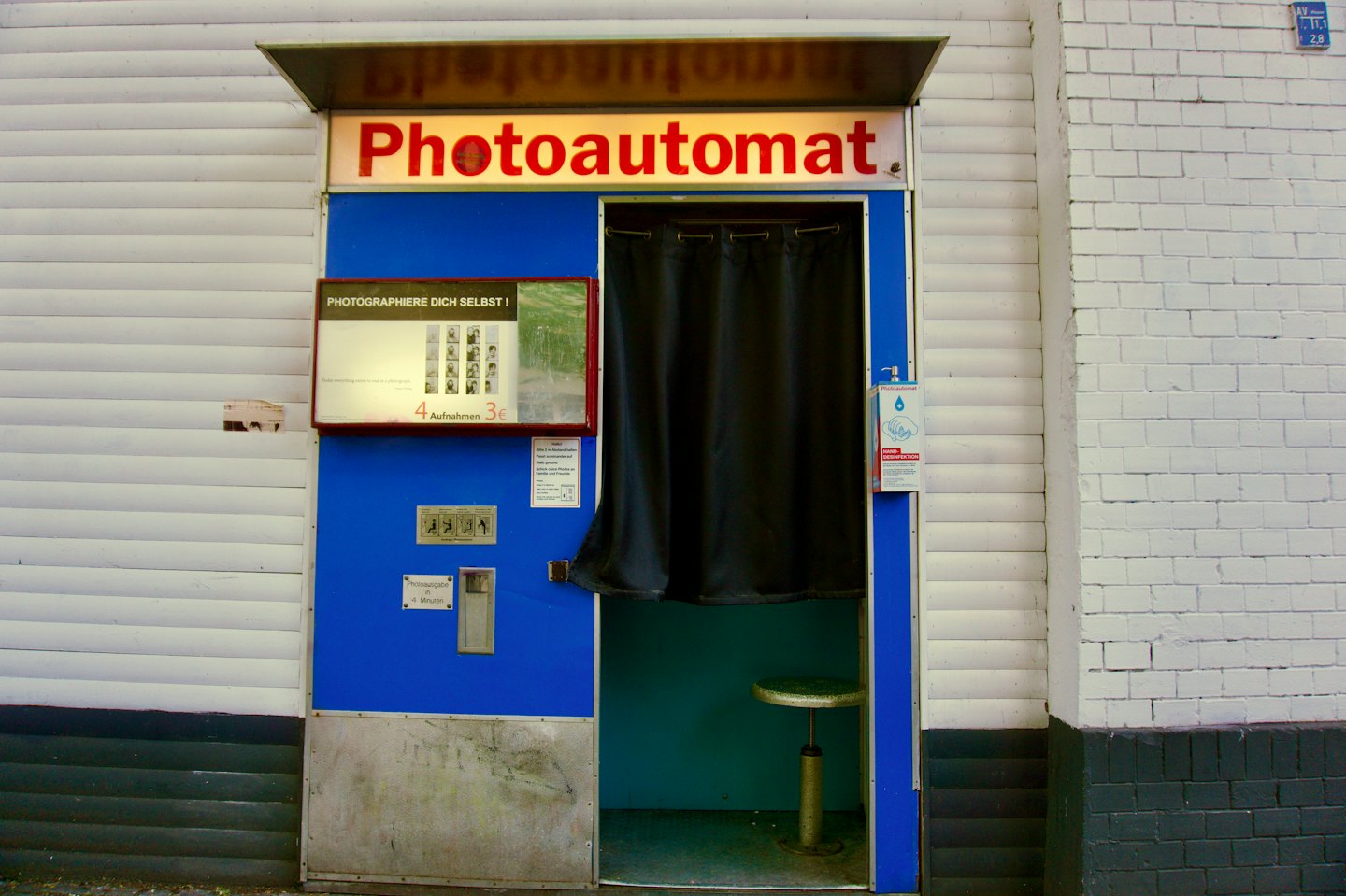 Cabine photo vintage bleue avec enseigne rouge en extérieur.